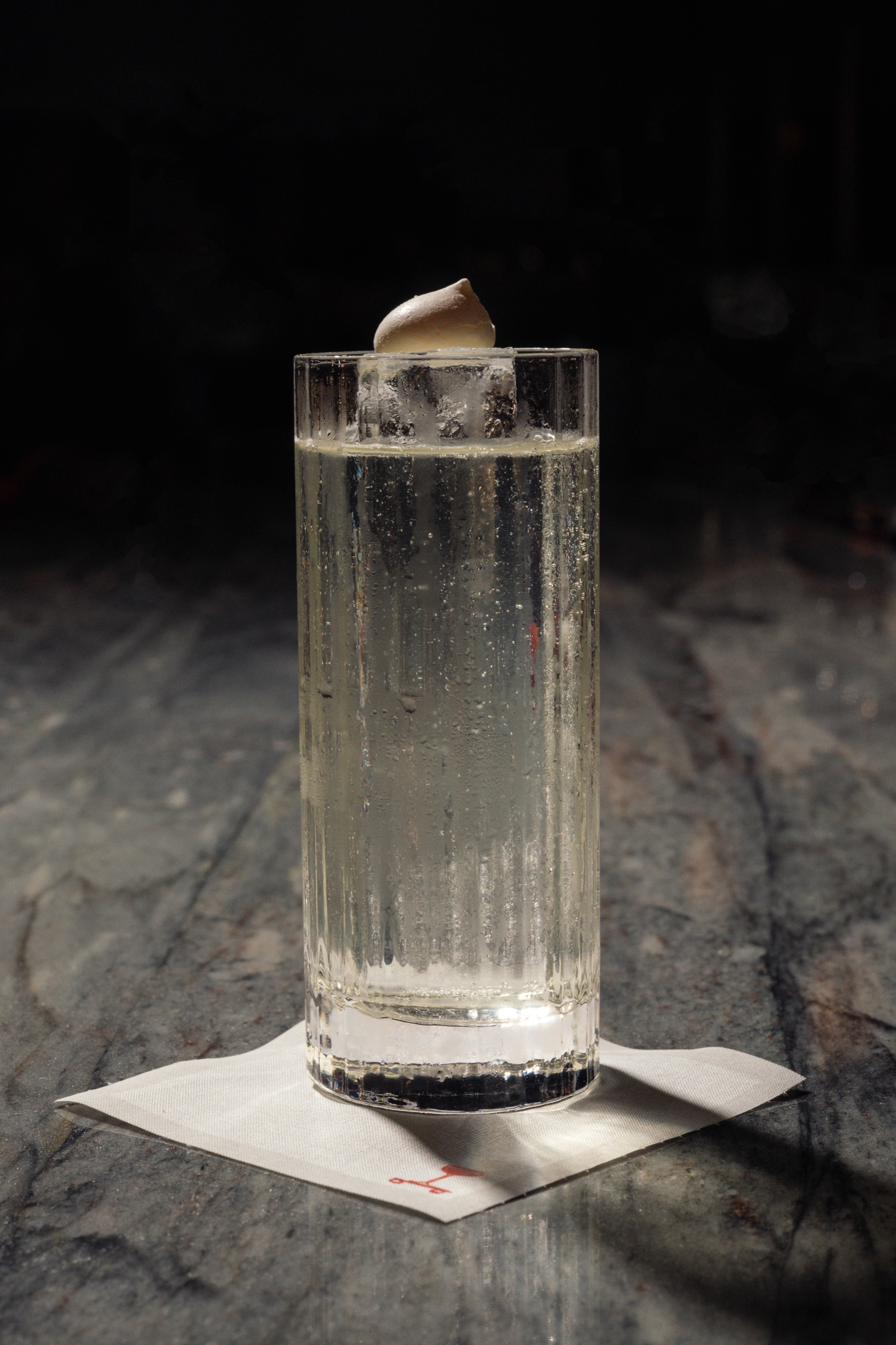 Tall clear cocktail with meringue garnish on marble