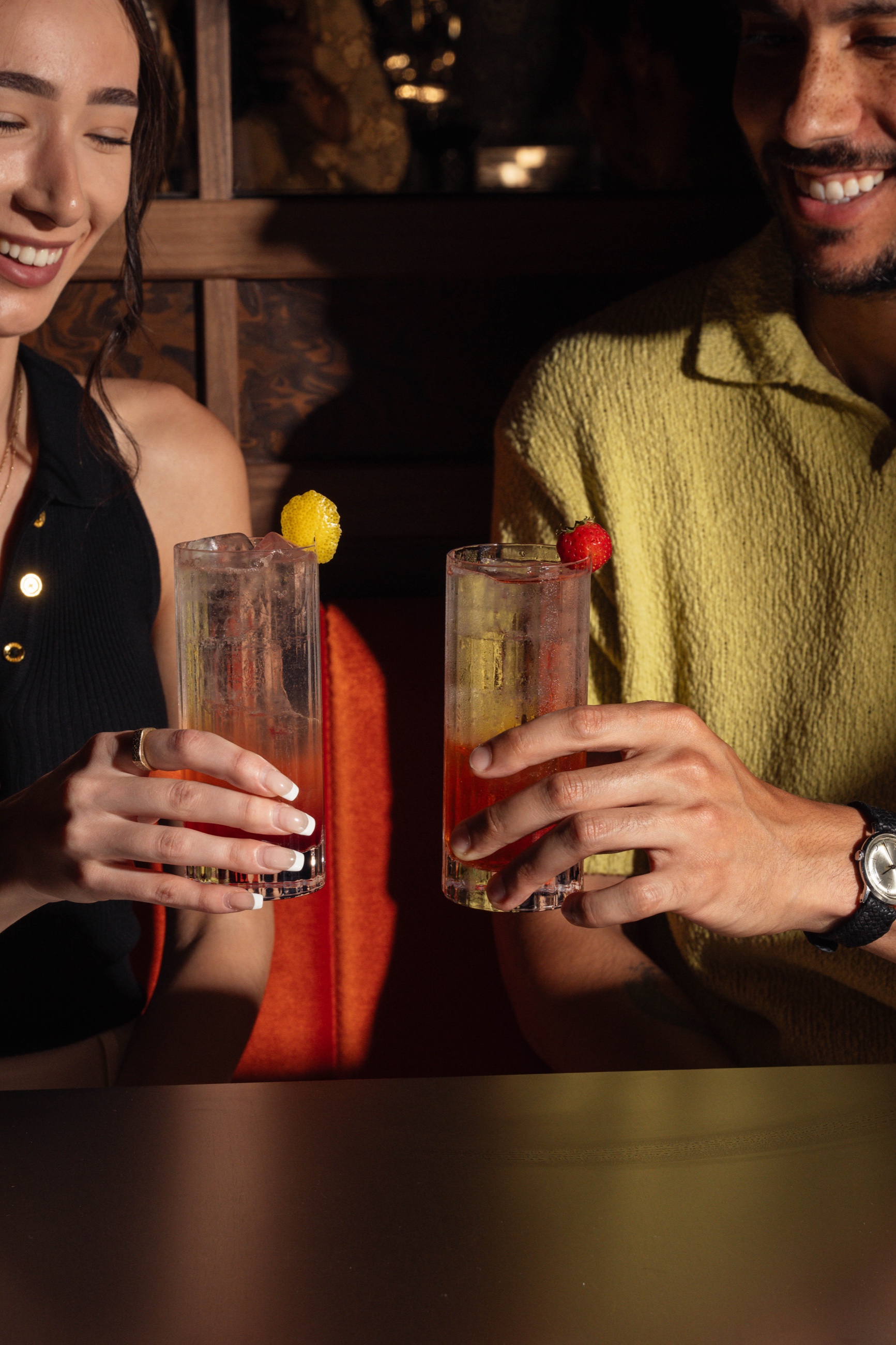 Couple laughing with cocktails in warm booth light