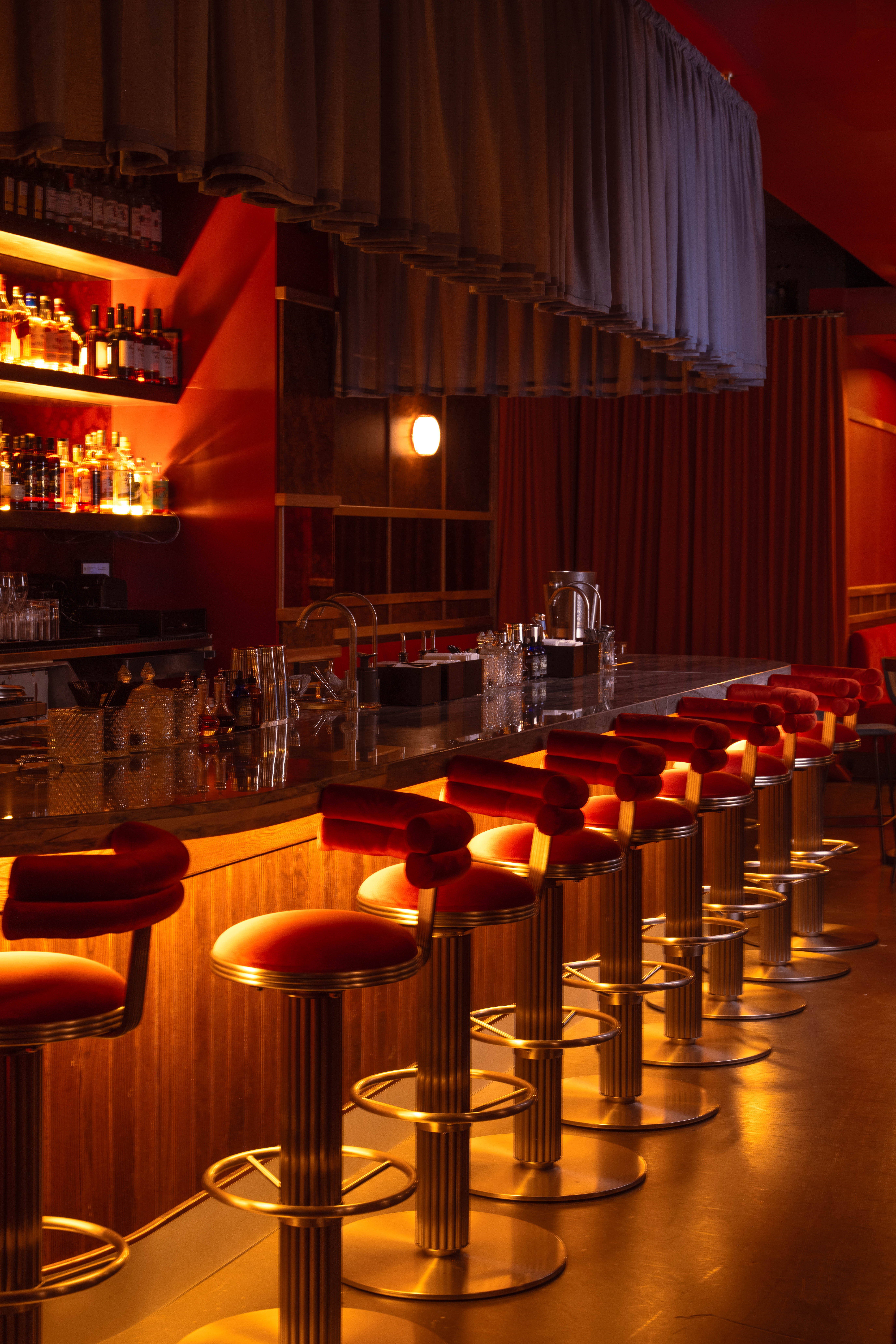 Long bar with red velvet stools under warm amber light