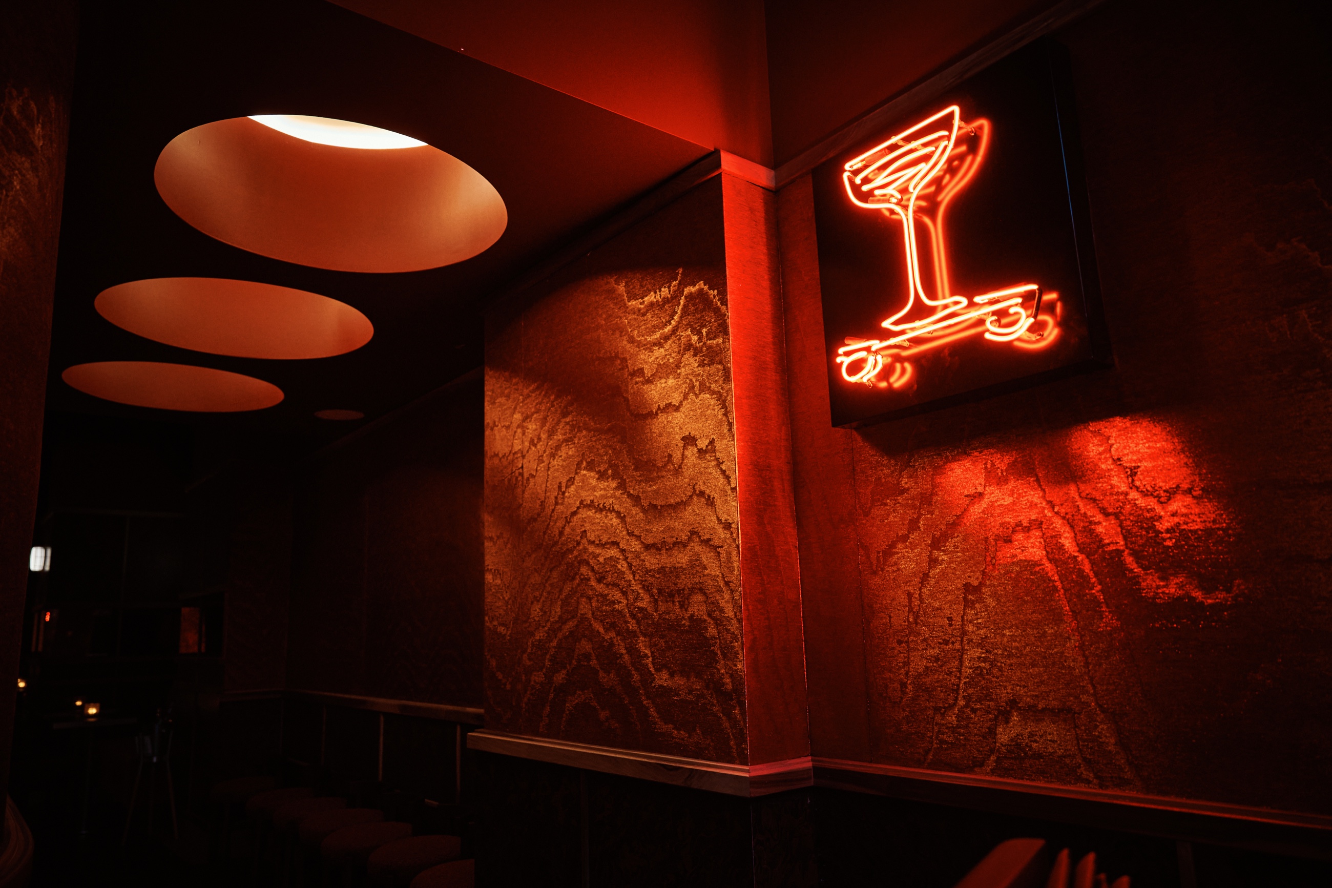 Neon cocktail sign glowing against amber-lit wall
