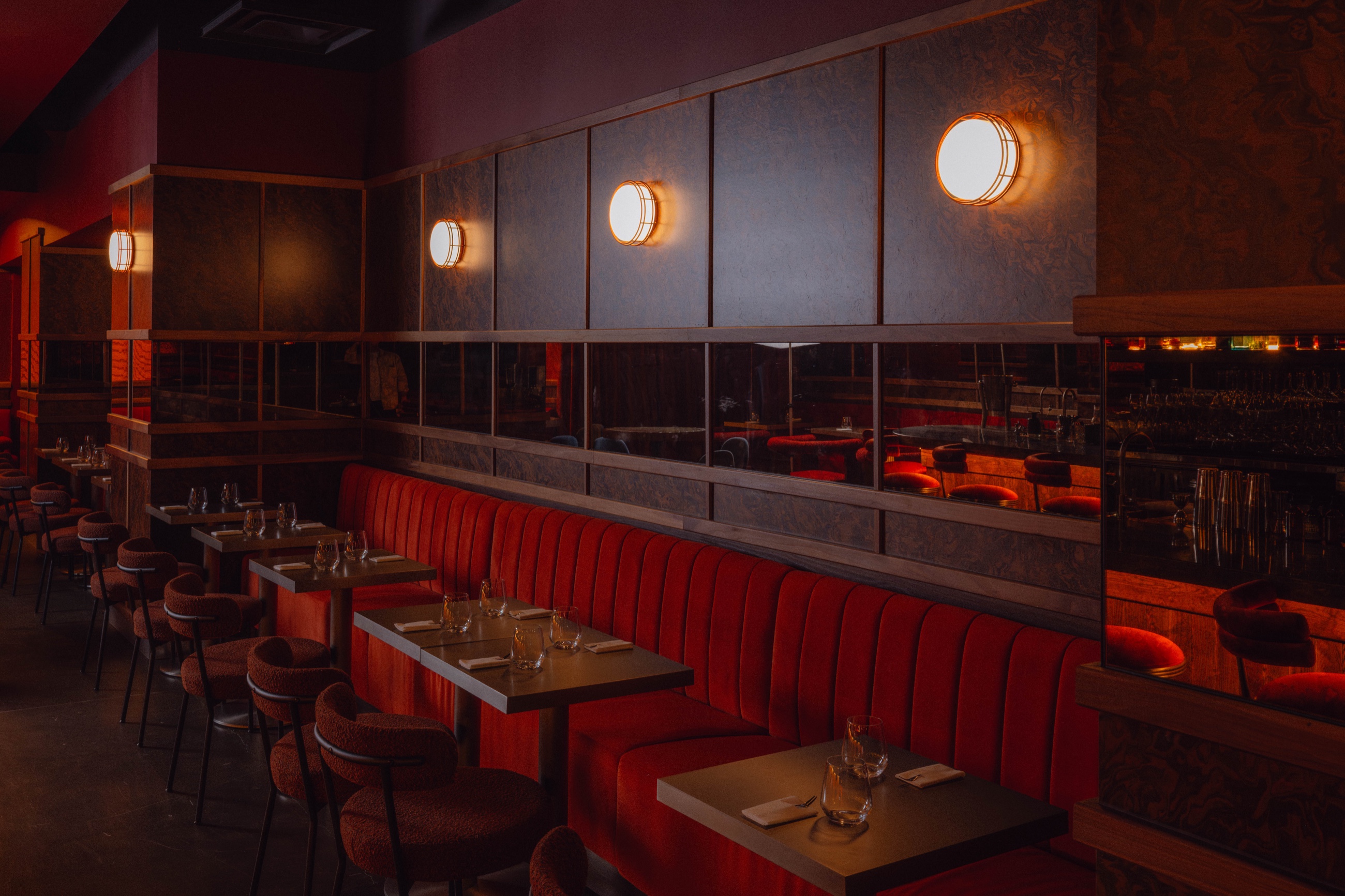Red velvet banquette with mirrored panels and warm sconces